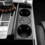 Center console with two cup holders, wireless charging pad and USB slot, plus a gear selector panel on the left and a beaded necklace resting near the shifter area.