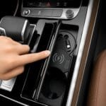 In-car center console showing a wireless charging pad with a smartphone being placed into the charging area next to cup holders and control buttons